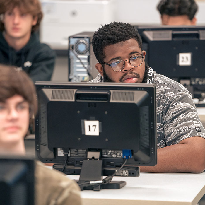 Male students sitting in classroom behind monitors