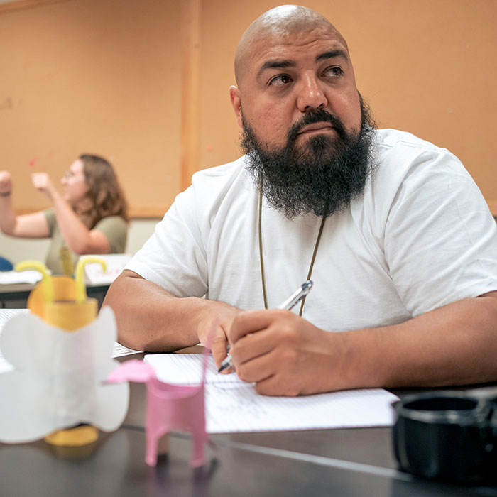 Male student listening intently in class while taking notes.