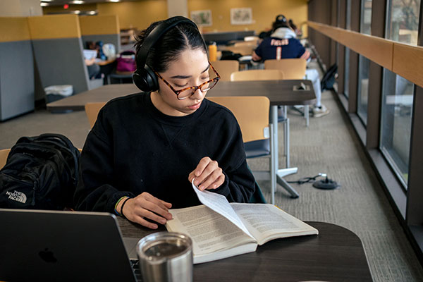 Female student wearing headphones and reading book in library