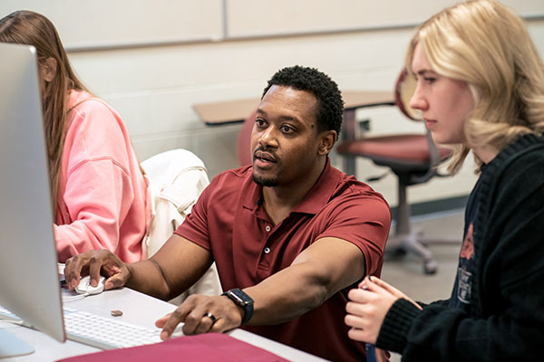 Male teacher explains concept at computer to female student