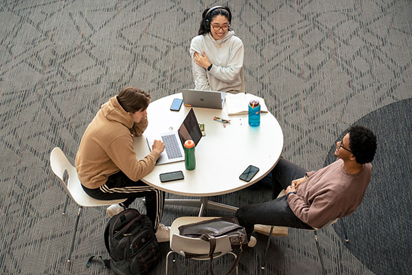 Three students sit around a table between class enjoying each other's company