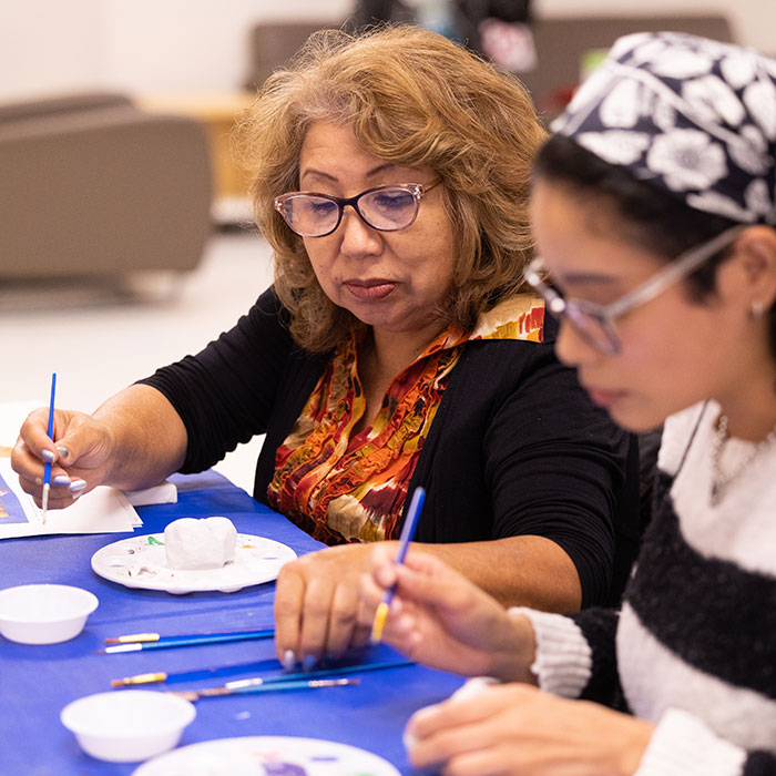 Two women work on an art project while seated at a table.