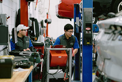 Two male students standing among equipment and cars on lifts.
