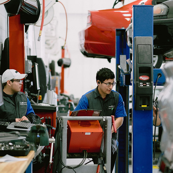 Two male students working on cars in the automotive lab