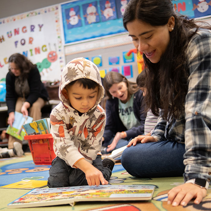 Child and teacher read a book together while sitting on the floor