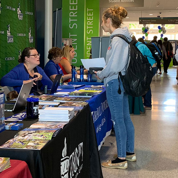 Female student standing at table, talking to college rep