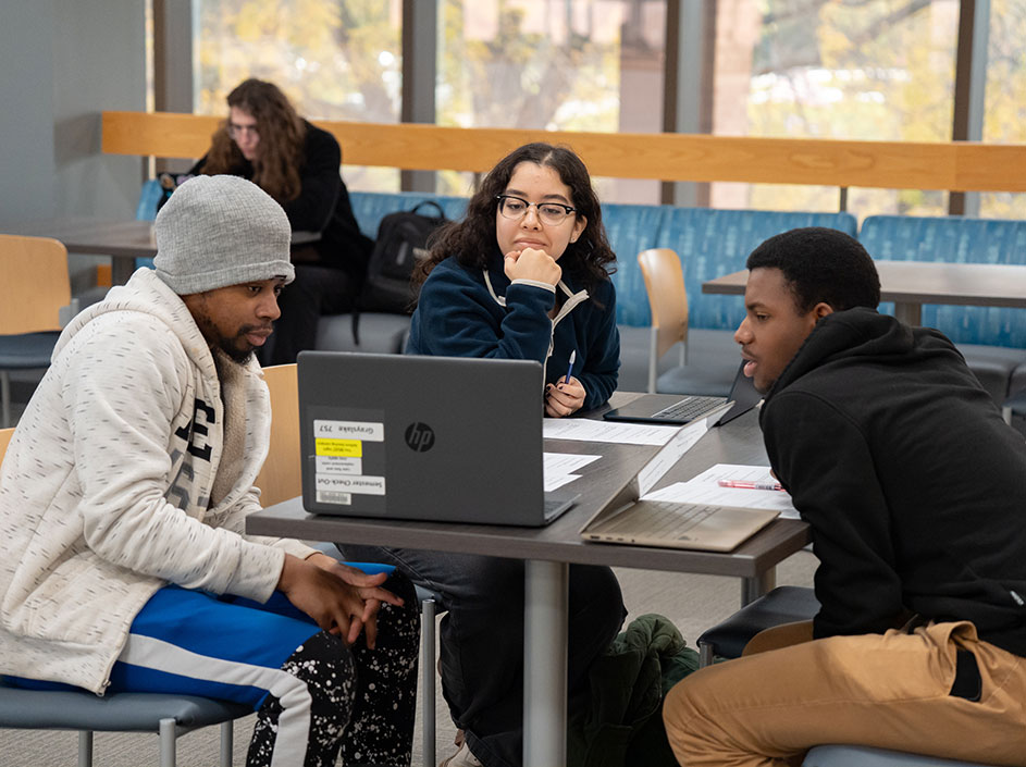 Three students looking at laptop while sitting at table