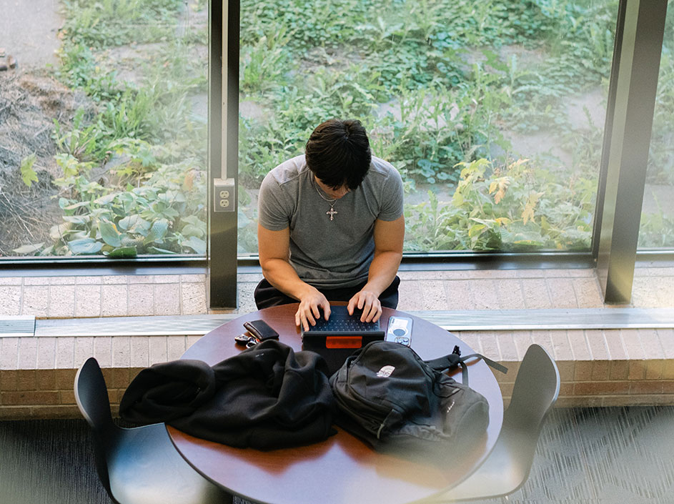 Student working on laptop near window
