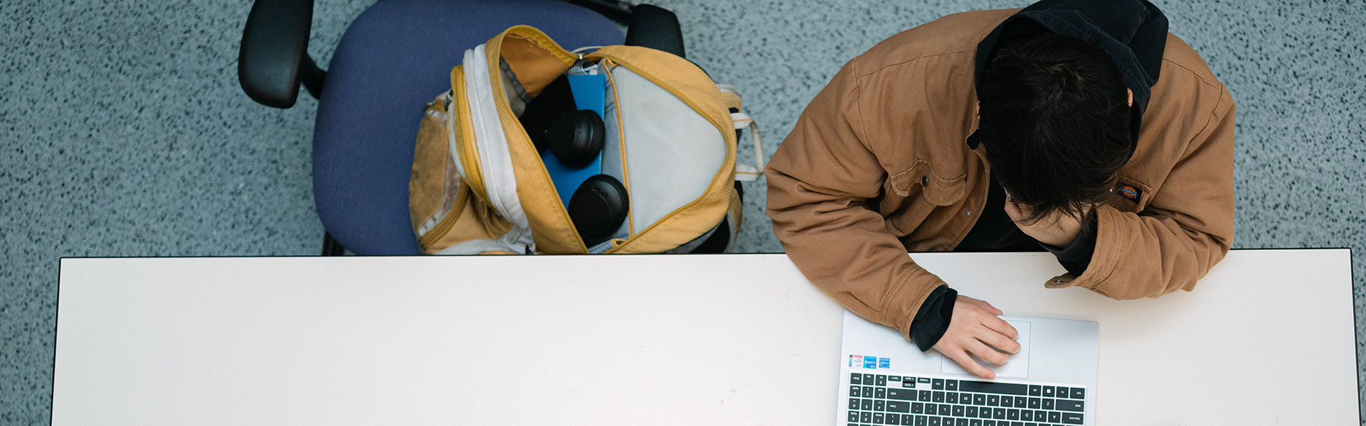 Top-down view of student looking at laptop with open backpack nearby