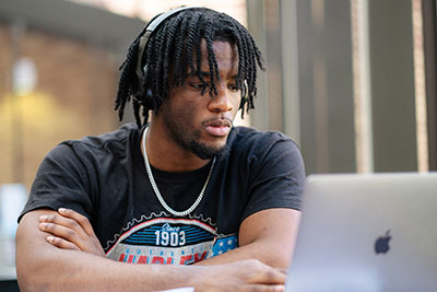 Male student wearing headphones, looking at laptop