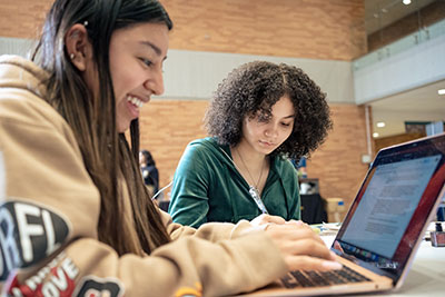 Two female students working on laptop, writing on paper