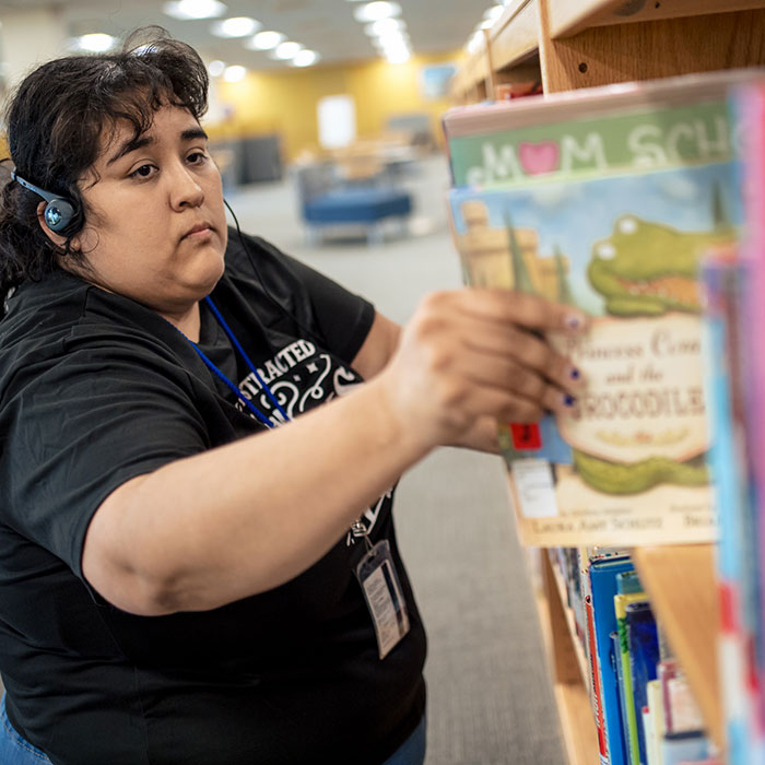A woman pulling a book from a library shelf.