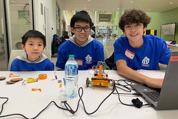 Three young boys sitting at table with laptop and mini robot