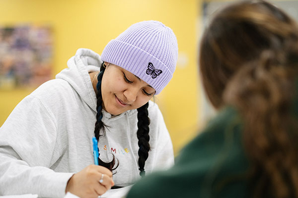 Female student wearing purple cap, writing in notebook