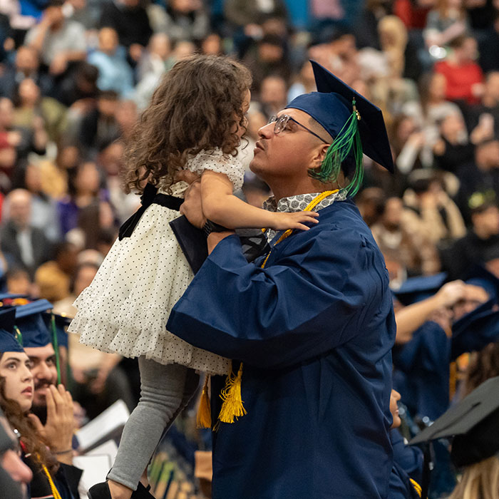 Male graduate celebrates with young daughter at commencement ceremony.