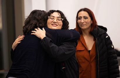Two female students hugging while a third looks on supportively