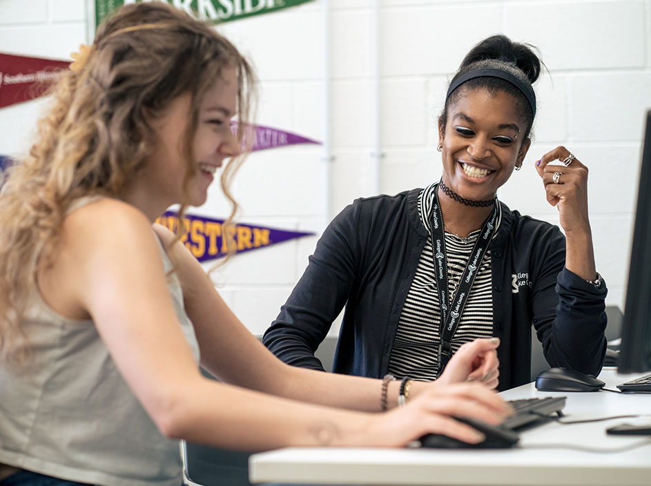 Female student and advisor exploring transfer options on computer with college pennants in background