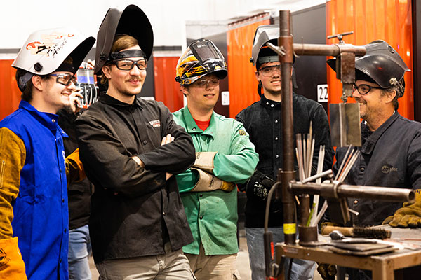 Students in welding gear listen to instructor.